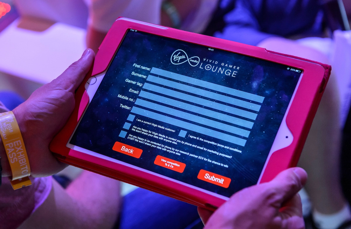 Close-up of a tablet screen displaying a registration form for a Gamer Lounge at a MatterXP event, held by a participant wearing an exhibitor pass. The form includes fields for personal information such as name, gamer tag, and email, with options to consent to terms and marketing communication.